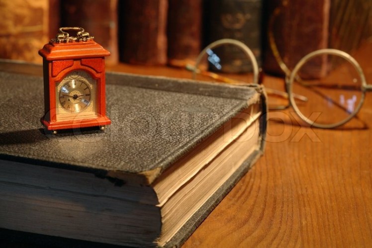 1617345-vintage-still-life-small-wooden-clock-standing-on-old-book-on-background-with-books-and-spectacles